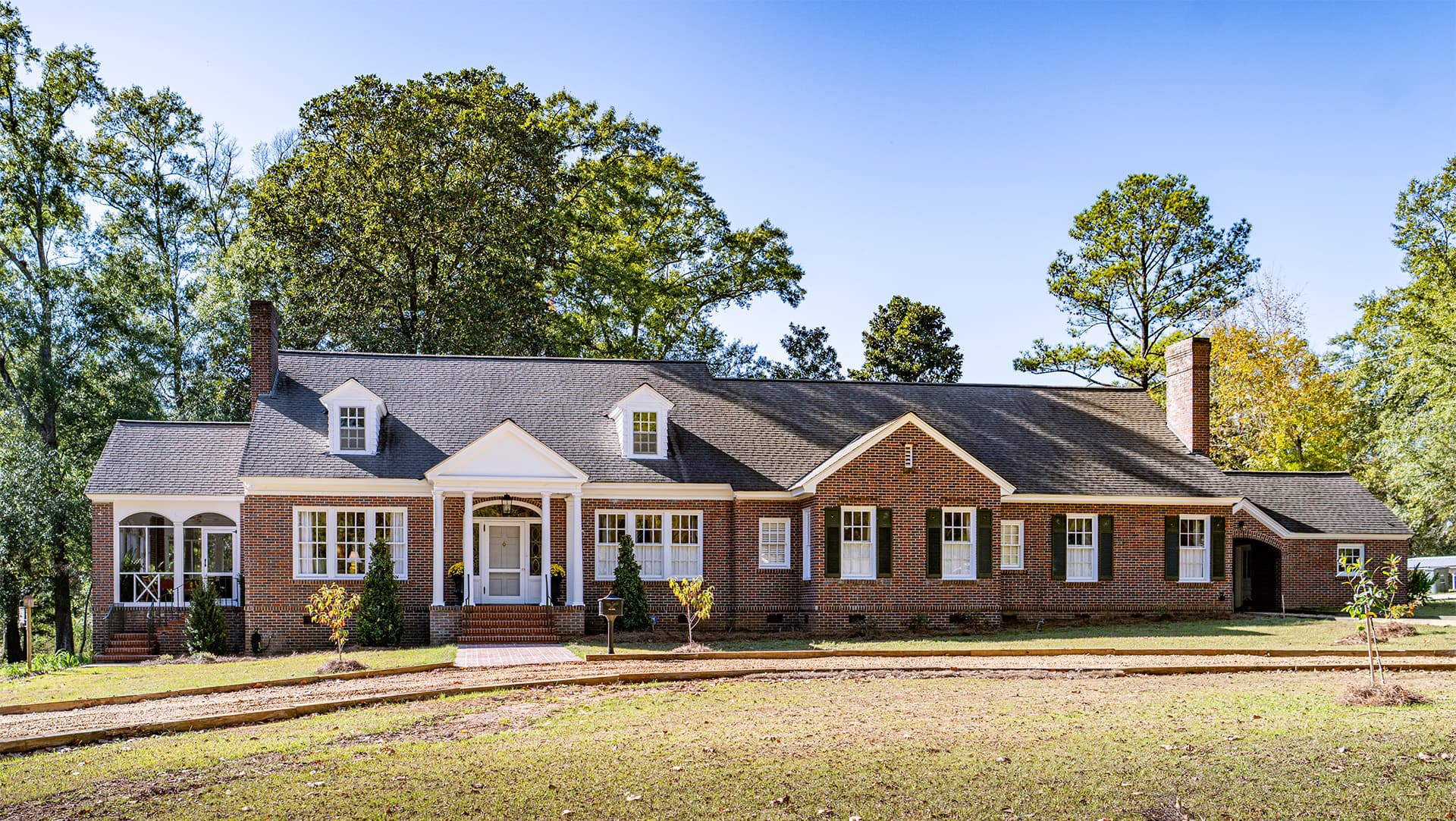 A large, brick house with a front porch, surrounded by trees and a grassy lawn.