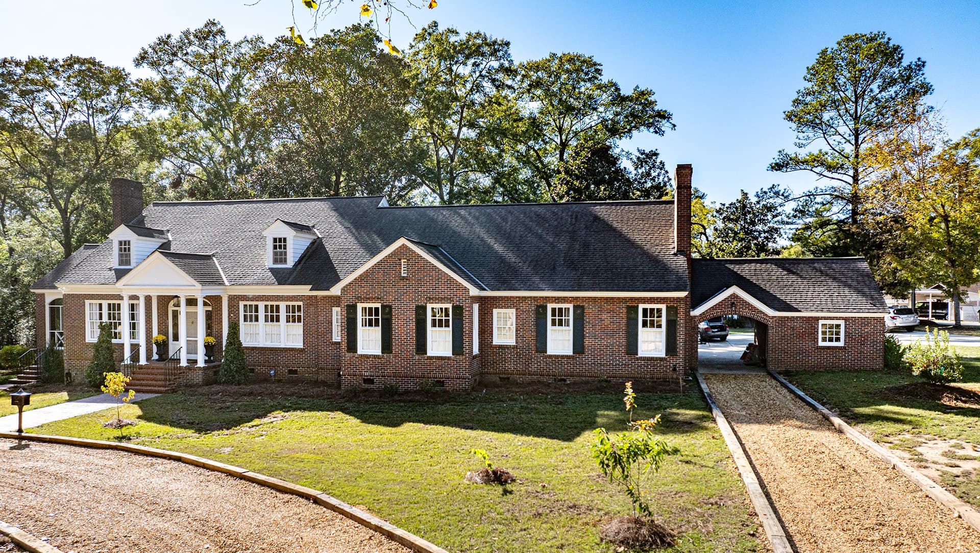 A large, brick-front house with a manicured lawn and trees in the background.