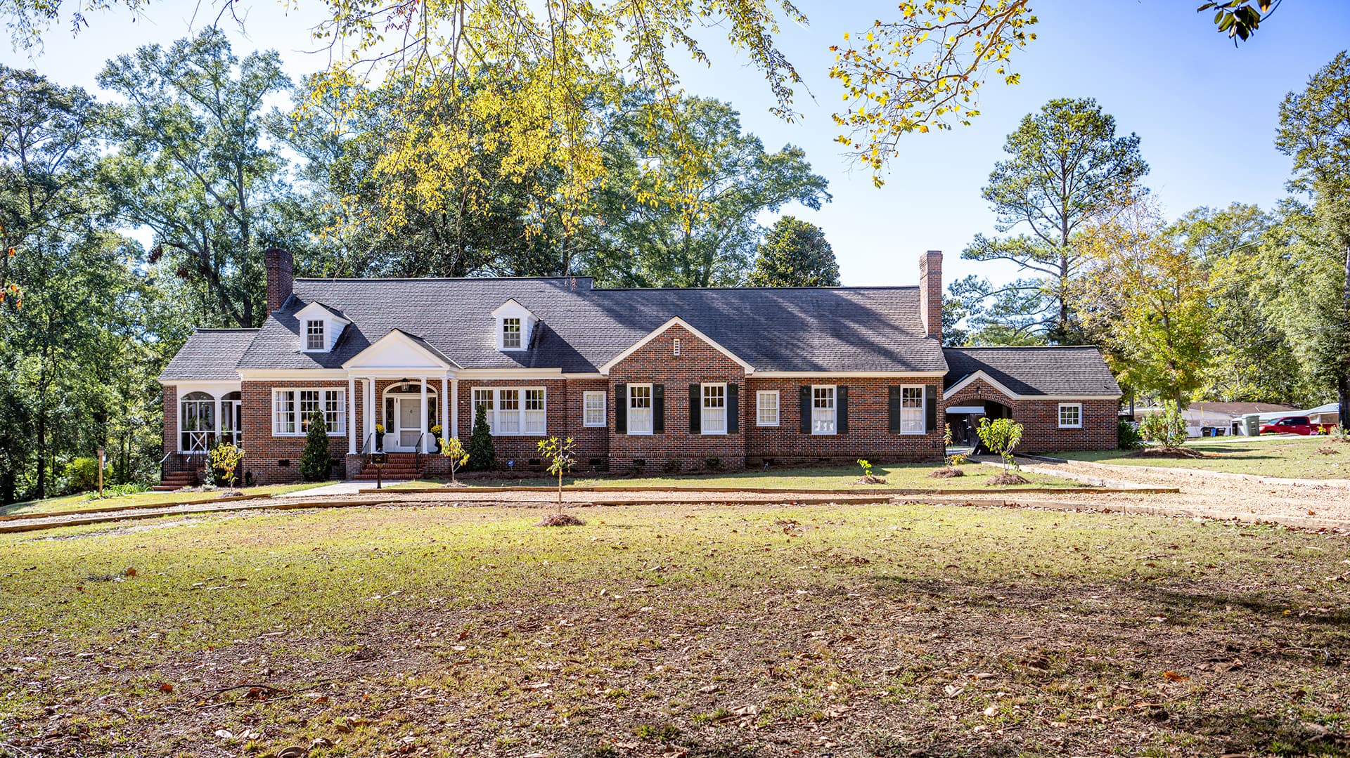 A large, brick-front home with a sloping roof, surrounded by a grassy yard and trees.