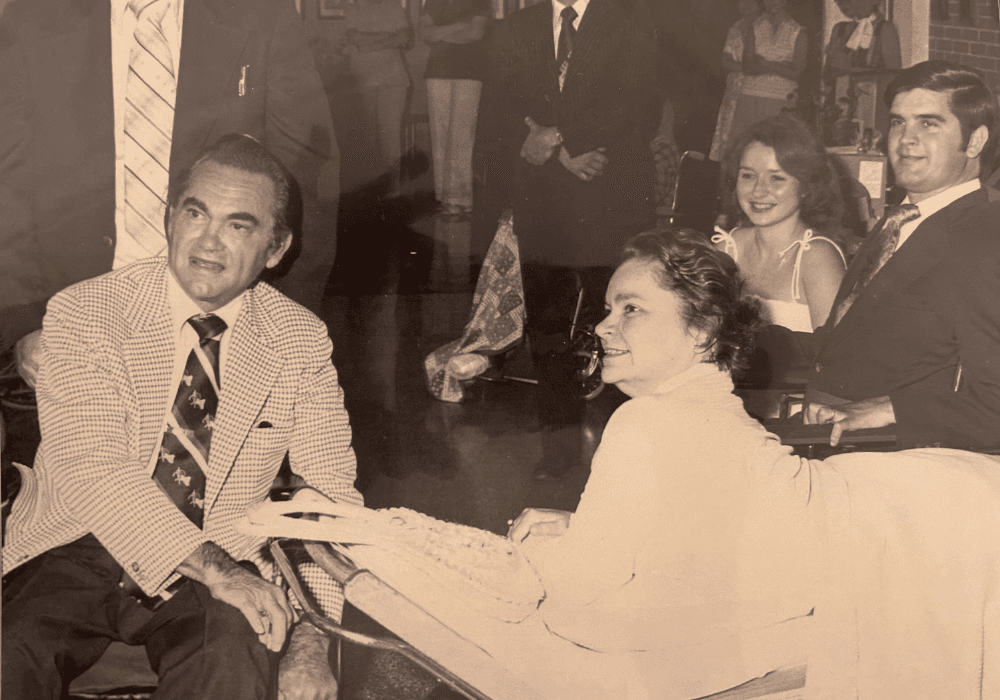 A group of four people, including two men and two women, are seated together in a social setting.