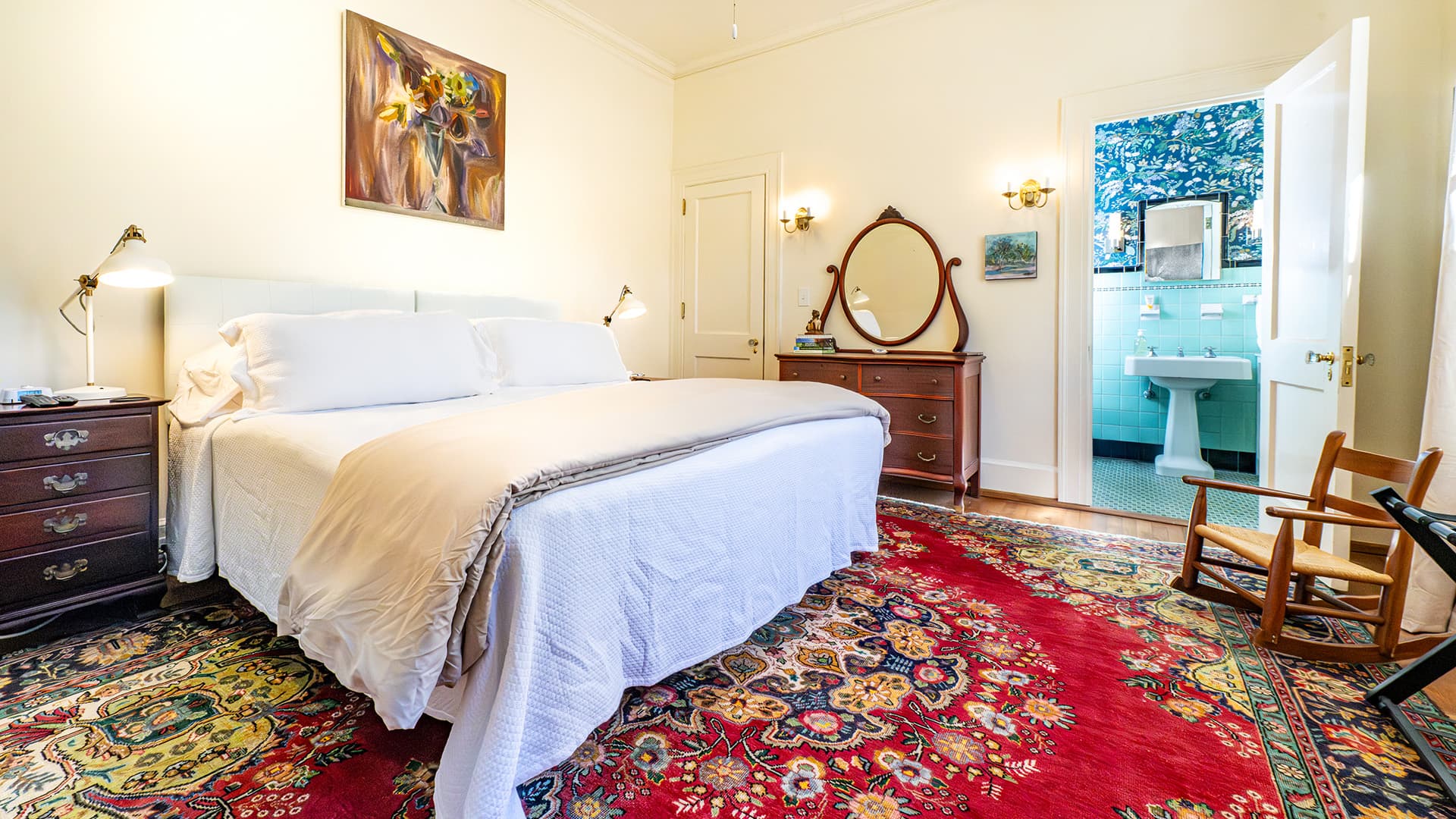 A cozy bedroom featuring a large bed, antique furnishings, and a view into a bathroom.