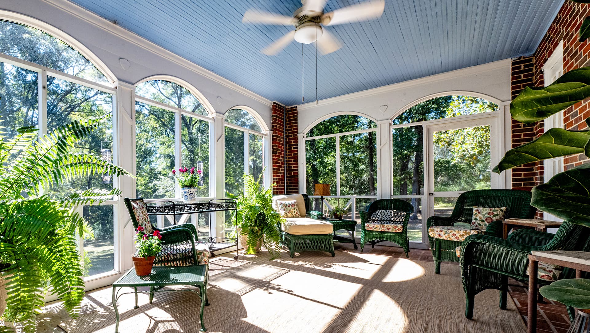 A bright sunroom featuring green chairs, plants, and large windows.